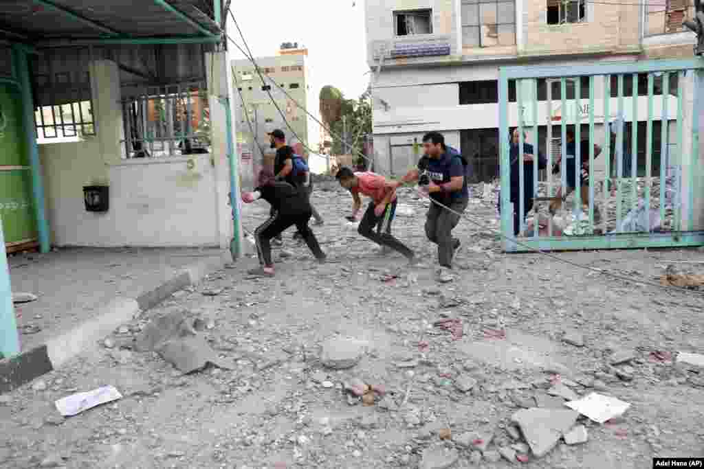 Палестинці, журналісти та інші люди, біжать, щоб сховатися під час ізраїльського авіаудару по верхніх поверхах комерційної будівлі біля Міністерства охорони здоров'я в місті Газі в понеділок, 17 травня 2021 року. (AP Photo / Adel Hana)