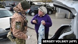 Український прикордонник оглядає автомобіль і перевіряє паспорт жінки, яка прямує на територію, непідконтрольну Києву, в пункті пропуску поблизу села Новотроїцького Донецької області