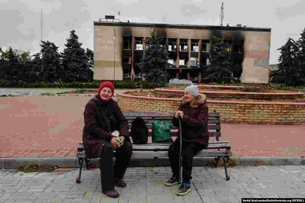 Жителі Ізюму в центрі міста. Не на камеру багато хто з місцевих жителів розповідає про окупацію, голодні смерті і як за їжу розбирали завали під керівництвом російських військових. Позаду спалена  будівля місцевої міськради, вересень 2022  року / Праворуч: початок жовтня 2024-го. Більшість нинішніх мешканців Ізюму – це люди пенсійного віку. Молоді й активні повертаються неохоче. За словами місцевих жителів, в Ізюмі дуже повільно йде відновлення пошкодженого житла. Через це будь-які інші ремонти, що відбуваються в місті, наприклад, будівлі мерії в центрі, що здійснюється в межах цільової міжнародної програми, викликають невдоволення в місцевих. Адже навколо побите й обгоріле житло, початок жовтня 2024 року