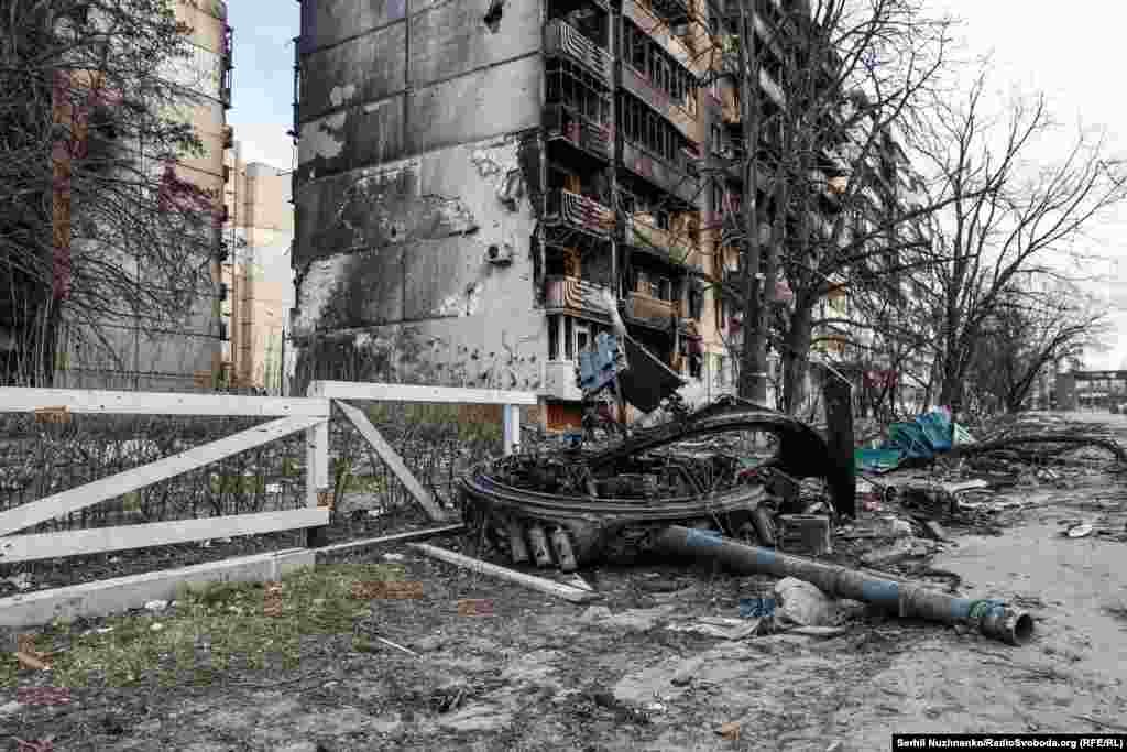 Пошкоджені житлові будинки на Гостомельському шосе, перед ними – знищена російська техніка. На фасаді першого будинку британський художник Бенксі пізніше зробив своє графіті.Потім ці будинки демонтували,. На їхньому місці – пустир. Роботу Бенксі перенесли на будинок поруч. Ліворуч фото від 7 квітня 2022, праворуч – березень 2025 року