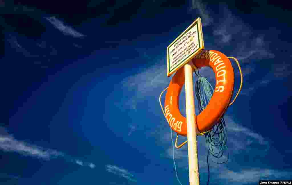 Спасательный круг на пляже в Феодосии. Объявление на нем гласит: «Спасение и оказание медицинской помощи не производится с 7 вечера до 8 утра. В это время лучше не тонуть и не находиться на пляже в плохом самочувствии»