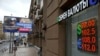 As the ruble plummets, Muscovites walk past a currency exchange office in the Russian capital alongside a billboard advertising military contracts for the country's armed forces.