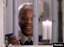 Нельсон Мандела держит свечу сквозь решетку тюремной камеры, в которой он был заключен на острове Роббен-Айленд, 31 декабря 1999 года