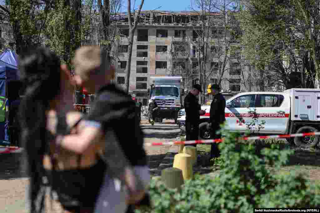 Жінка з дитиною на фоні місця удару.Внаслідок російського удару в ніч на 24 квітня в Святошинському районі Києва був зруйнований житловий будинок. 12 людей загинули, 90 – зазнали поранень. Рятувальна операція тривала до ранку 25 квітня