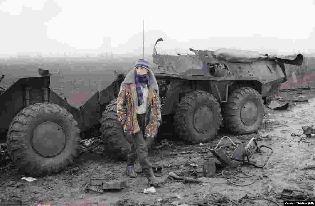 Чеченец, стоящий перед обломками российского бронетранспортера, который уничтожен в результате столкновения чеченских повстанцев и российских войск, смотрит на российский блокпост. Местность к западу от Грозного, 31 января 1995 года