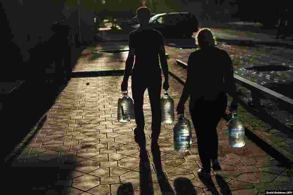 Подружжя несе пляшки з водою, які наповнили у магазині в Покровську, 4 серпня 2022 року.  У багатьох районах Донецької області немає регулярного водопостачання