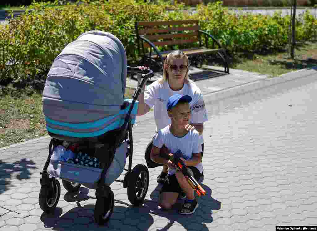 Хлопчик із іграшковою рушницею стоїть на колінах разом зі своєю мамою під час похорону українського військового в Київській області 17 липня