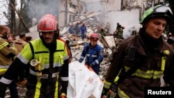 Рятувальники виносять тіла загиблих людей, яких знайшли під завалами знищеного російського ракетою під'їзду житлового будинку у Києві. 31 липня 2025 року