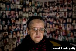 Хайра Чатич, яка втратила чоловіка й сина під час масового вбивства в Сребрениці у 1995 році, на тлі фотографій загиблих і зниклих безвісти