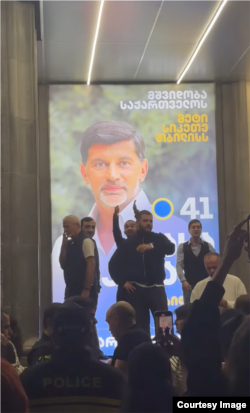 ათუკა წიკლაური ხელებაწეული ჩანს კალაძის ბანერის ფონზე.