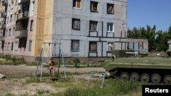 Хлопчик на гойдалці біля пошкодженого під час боїв будинку у Авдіївці. 7 червня 2015 року