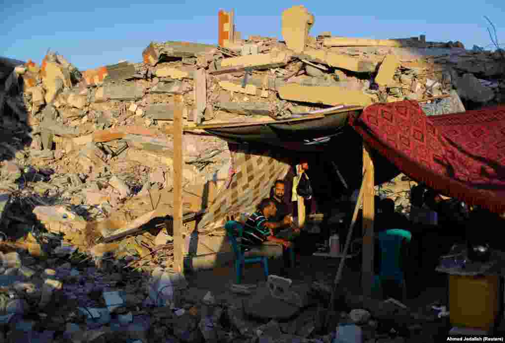 Люди сидять біля руїн їхніх будинків, зруйнованих під час боїв між Ізраїлем та екстремістським угрупованням «Хамас» у Смузі Гази, 23 травня 2021 року
