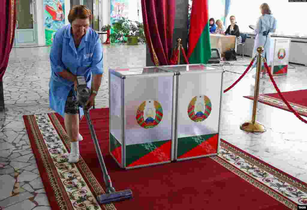 Прибиральниця чистить пилососом килим біля виборчих урн в Мінську