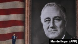 Президент США Дональд Трамп выступает на церемонии по случаю 75-й годовщины высадки союзных войск в Нормандии 5 июня 2019 года на фоне флага США и портрета президента времен Второй мировой Франклина Д. Рузвельта