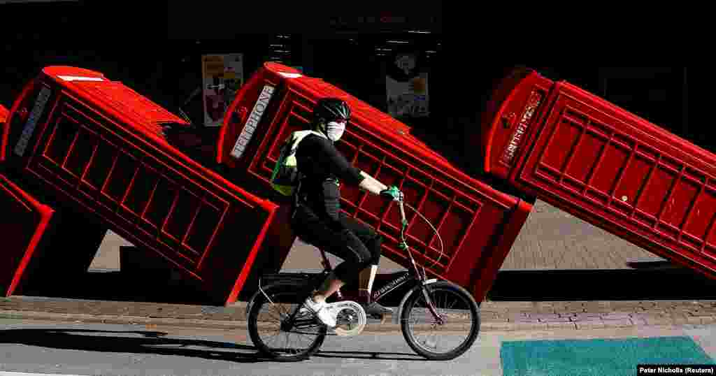 Велосипедист їде в захисній масці повз інсталяцію «Out of Order» скульптора Девіда Мача. Дванадцять червоних телефонних будок класичної моделі, які є настільки ж упізнаваним символом Великої Британії, як і поштові скриньки та двоповерхові автобуси, покладені на бік за «принципом доміно»