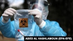 پرسنل وزارت بهداشت سرزمینهای فلسطینی نمونه تست کرونا یک کارگر بازگشته از اسرائیل را داخل کیسه پلاستیکی میگذارد.