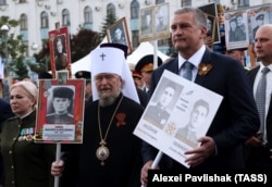 Митрополит Сімферопольський і Кримський УПЦ (МП) Лазар (посередині) і керівник окупованого Росією Криму Сергій Аксенов (праворуч) під час акції пам'яті «Безсмертний полк». Окупований Сімферополь, 9 травня 2017 року