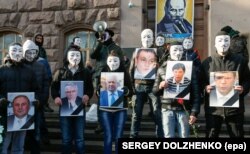 Революція гідності, Київ, 6 лютого 2014 року. Члени «Руху Гая Фокса» тримають портрети соратників президента Віктора Януковича під час акції «Похорон Партії регіонів» біля штабу партії у столиці України. Портрет Михайла Чечетова другий зліва