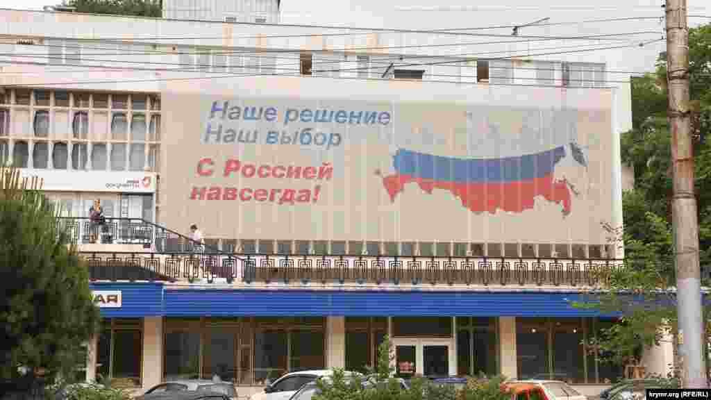 С утра на административных зданиях города коммунальные службы развесили российские флаги.  Плакат на стене здания российского Многофункционального центра по оказанию государственных услуг