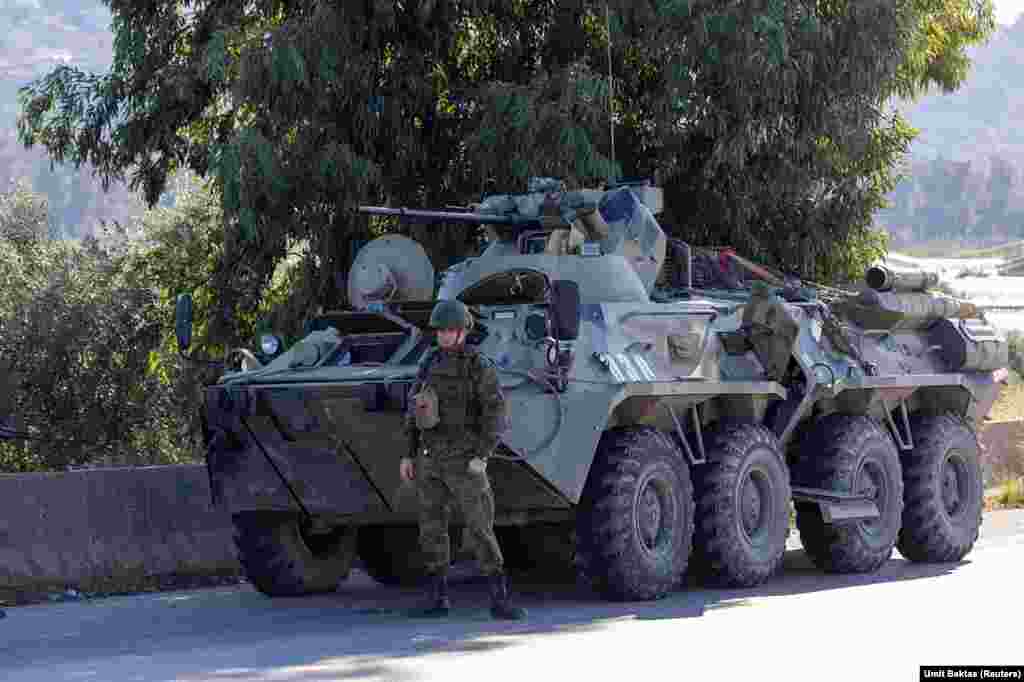 Російський солдат охороняє броньовану військову машину, у якої відмовив двигун. Біля авіабази Хмеймім. 15 грудня 2024 року. Колишній президент Сирії Башар Асад у письмовій заяві, в якій описує свою втечу з країни через наступ повстанців, стверджує, що спочатку його вивезли з Дамаска на базу Хмеймім. Звідти 8 грудня його переправили до Росії. Перед цим ця російська авіабаза «зазнала атаки безпілотників»