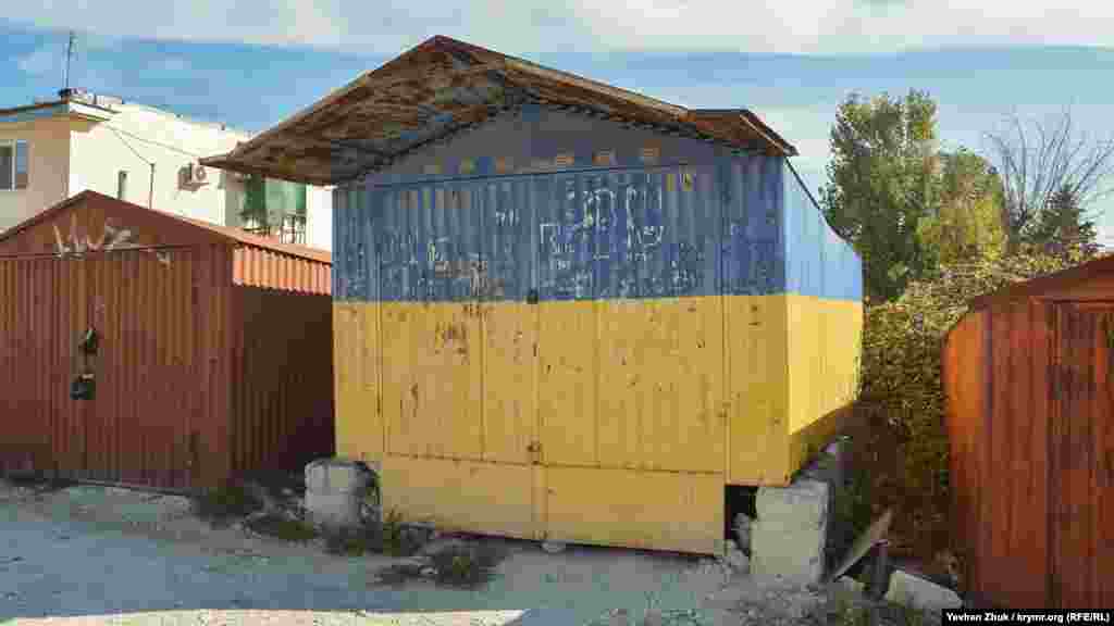 Когда-то в самом центре села была и такая торговая точка: до 2014 года этот сине-желтый гараж стоял на импровизированной «центральной площади». После аннексии Крыма он стал «мешать» российским властям Крыма – хозяин был вынужден его убрать вглубь местного гаражного кооператива, однако перекрашивать не стал