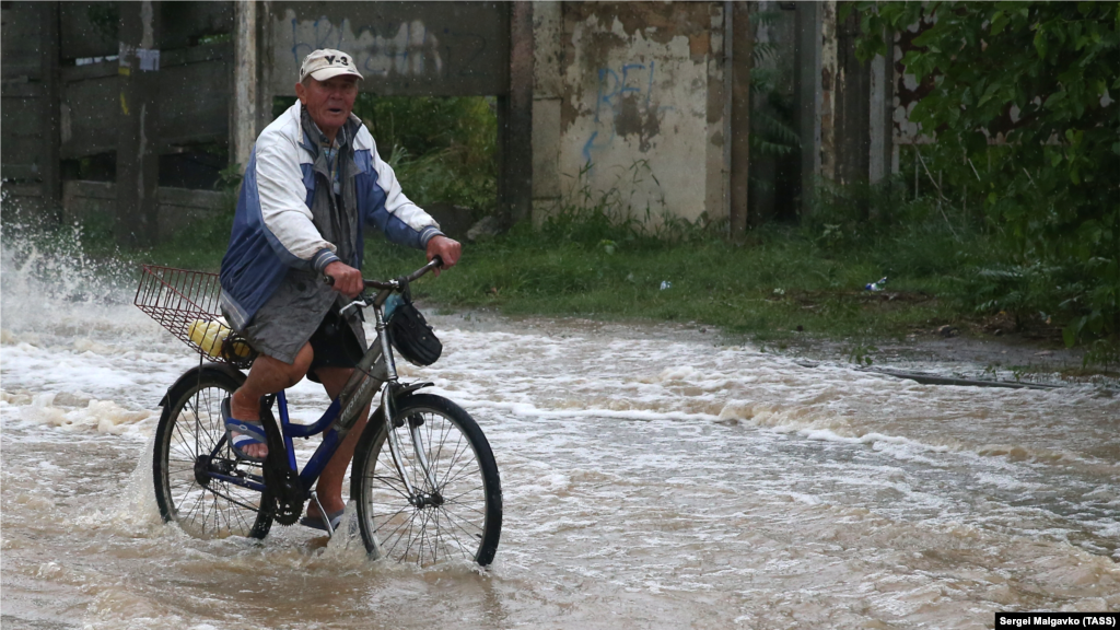 Мужчина едет на велосипеде по затопленной улице в Керчи. 13 августа 2021 года в связи с выпадением обильных осадков оказались затоплены центральные улицы Керчи. В Ленинском районе Крыма в результате ливней река Катерлез, которая впадает в речку Мелек-Чесме в Керчи, сильно наполнилась водой. Больше фото из Керчи – здесь