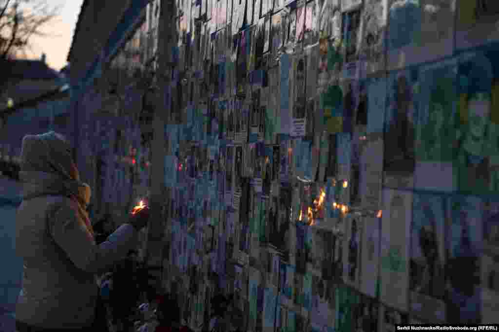 Жінка запалює свічку біля «Стіни пам’яті на Михайлівській площі 