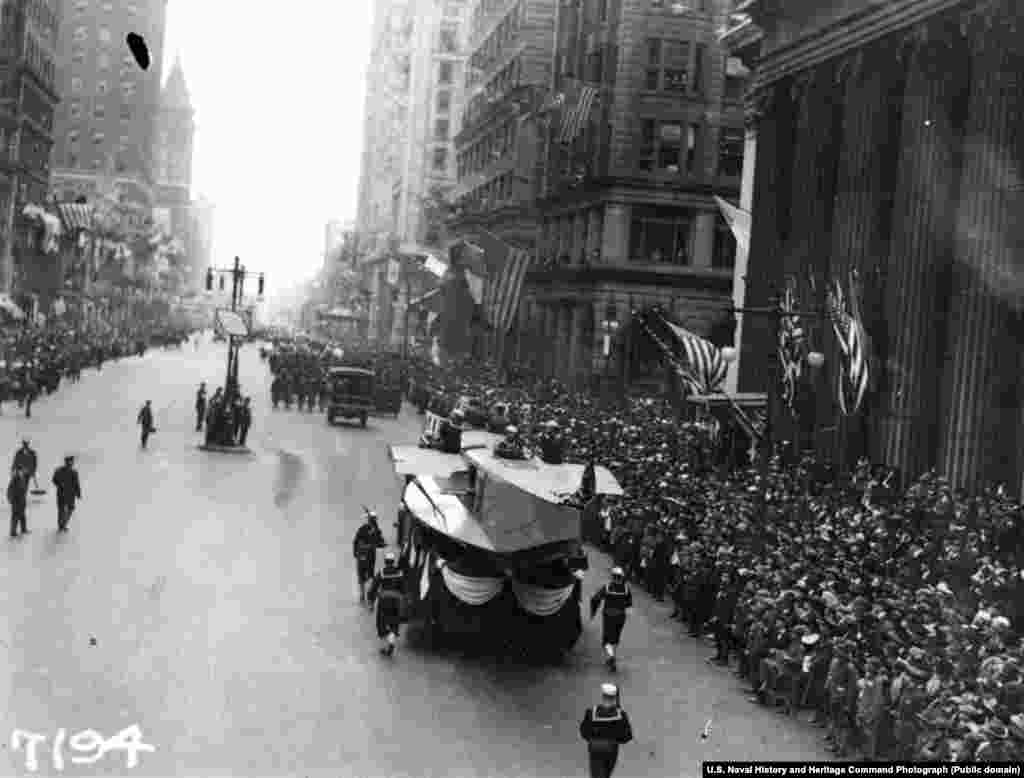 Мобільний стенд Заводу морської авіації рухається по Броуд-стріт у центрі Філадельфії під час параду, присвяченого «Законові про позики свободи», за яким спостерігають юрби людей. Позики свободи – це облігації, які видав уряд США, щоб оплатити витрати на війська коаліції під час Першої світової війни. Парад пройшов 28 вересня 1918 року. За день до параду в Філадельфії 118 осіб були хворі на «іспанку». Через кілька днів у місті стався масовий спалах хвороби