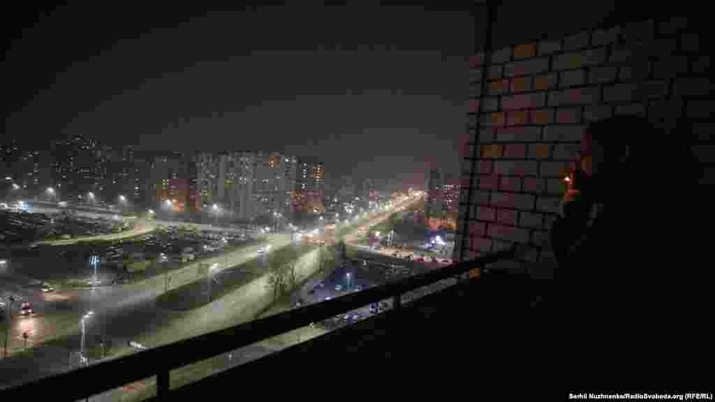 Чоловік курить на балконі багатоповерхівки в спальному районі «Позняки», дивлячись як місто накриває густий «туман»-смог