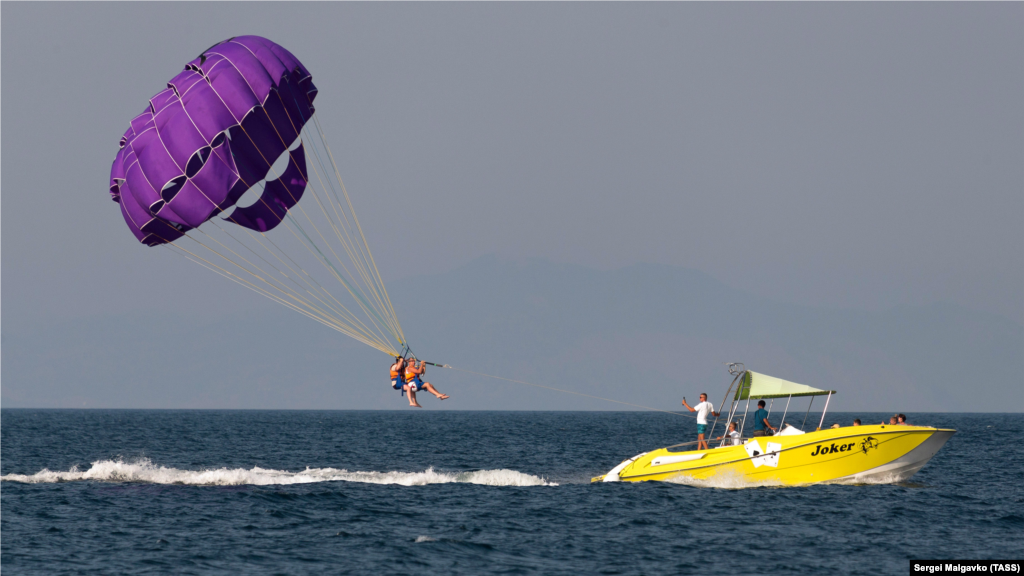 Отдыхающие занимаются парасейлингом в Черном море. Парасейлинг – это активный вид отдыха, во время которого человек поднимается над водой на специальном парашюте, прикрепленном с помощью троса к катеру или другому водному транспорту 