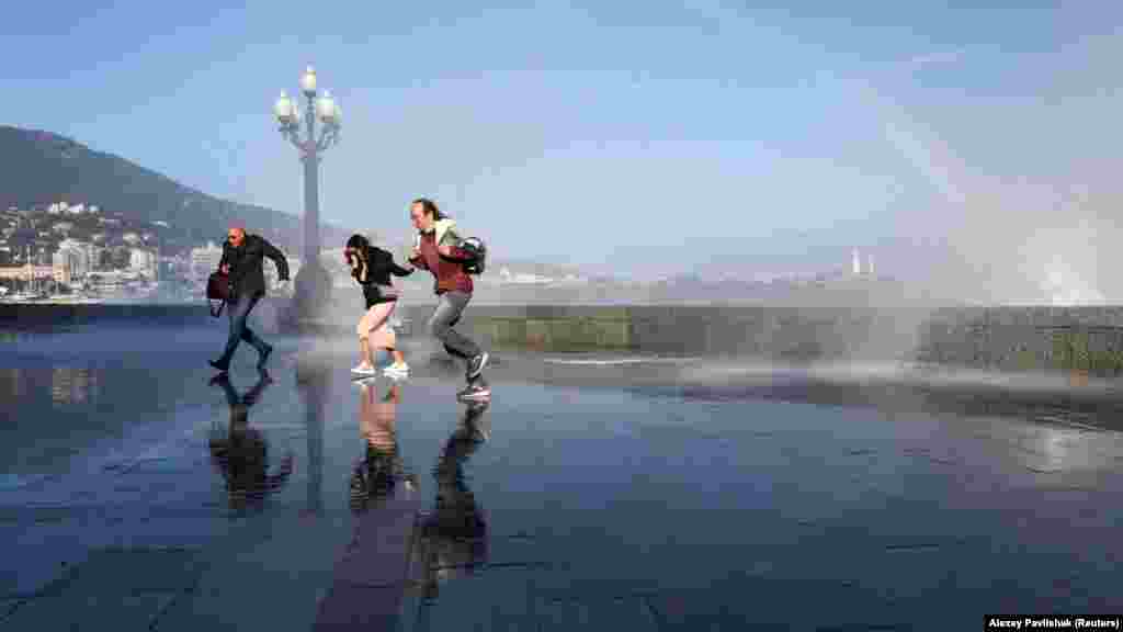 Люди бегут по набережной от водяных брызг 