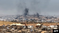 Це фото, зроблене з позиції на півдні Ізраїлю на кордоні з сектором Гази, показує ізраїльські танки та бульдозери, розгорнуті на тлі клубів диму над зруйнованими будівлями в Газі під час ізраїльського бомбардування, 17 травня 2025 року.