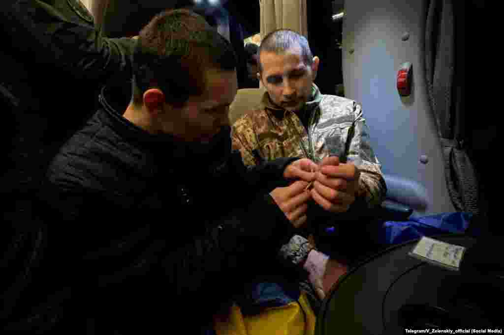 Звільнений з полону український захисник зав'язує на руку своєму побратиму жовто-блакитний браслет