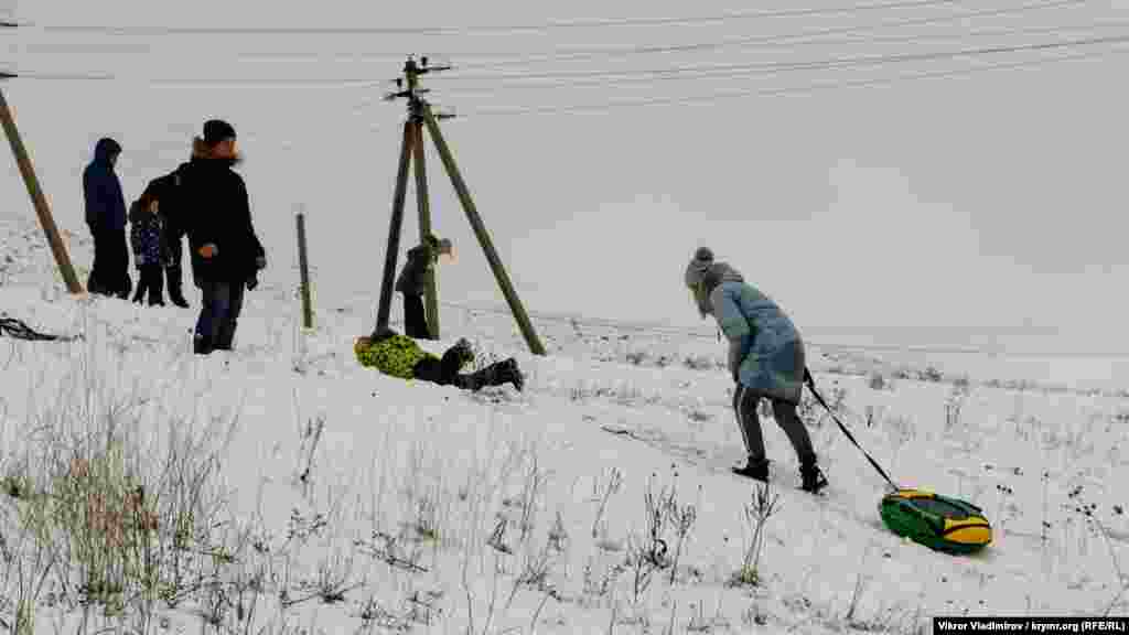 Дети катаются на надувных кругах («ватрушках») и традиционных санках