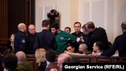 პენიტენციური სამსახურის თანამშრომლები რეზო კიკნაძეს სხდომათა დარბაზიდან აძევებენ.