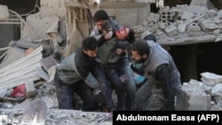 Сирийцы спасают ребенка после воздушного удара сил Асада в повстанческом городе Хамурия, в осажденном регионе Восточная Гута на окраине Дамаска, 21 февраля 2018 года
