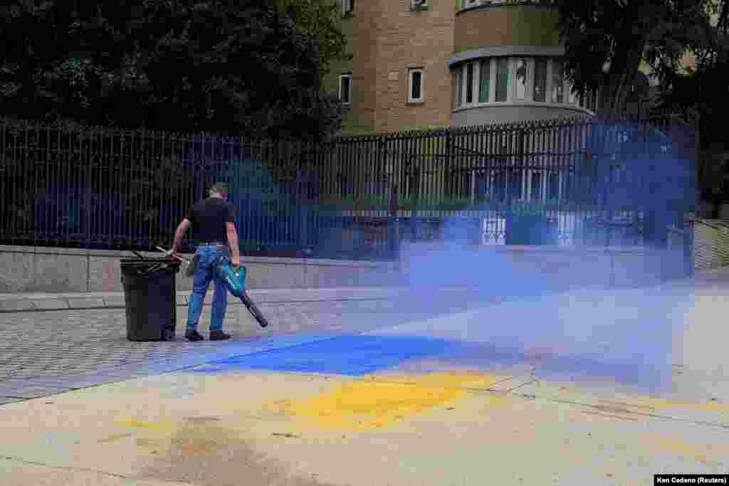 Мужчина очищает тротуар у посольства России в Вашингтоне от насыпанной на него синей и желтой порошковой краски. Это цвета флага Украины. США, округ Колумбия, август 2025 года