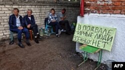 Місцеві жителі сидять біля таблички з написом «Цивільні в підвалі, військових немає» в підконтрольному Україні російському містечку Суджа Курської області, 16 серпня 2024 року