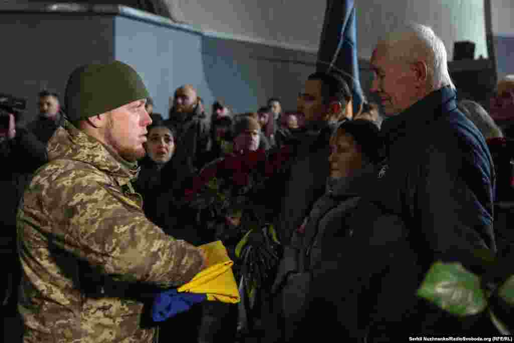 Військовий складає державний прапор і передає батькам загиблого зі словами: «Від імені Президента України, Верховного головнокомандувача Збройних Сил України, прийміть цей Прапор як символ держави, якій вірно й до кінця служив Ваш син