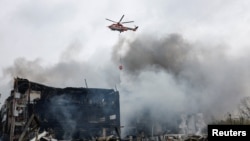 Гелікоптер намагається загасити пожежу у Києві, що виникла внаслідок російського повітряного удару. 25 жовтня 2025 року