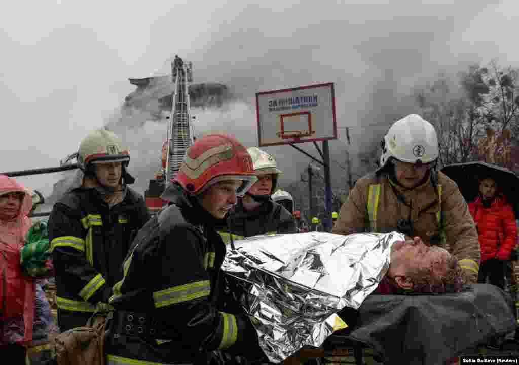 Рятувальники несуть поранену жінку, яку вдалося врятувати з-під завалів будинку, в який влучила російська ракета