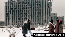 Жители Грозного проходят мимо разрушенного президентского дворца в Грозном. Февраль 1996 года