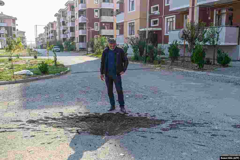 Мужчина смотрит на воронку на дороге в городе Тертер (Азербайджан), недалеко от линии фронта, 18 октября