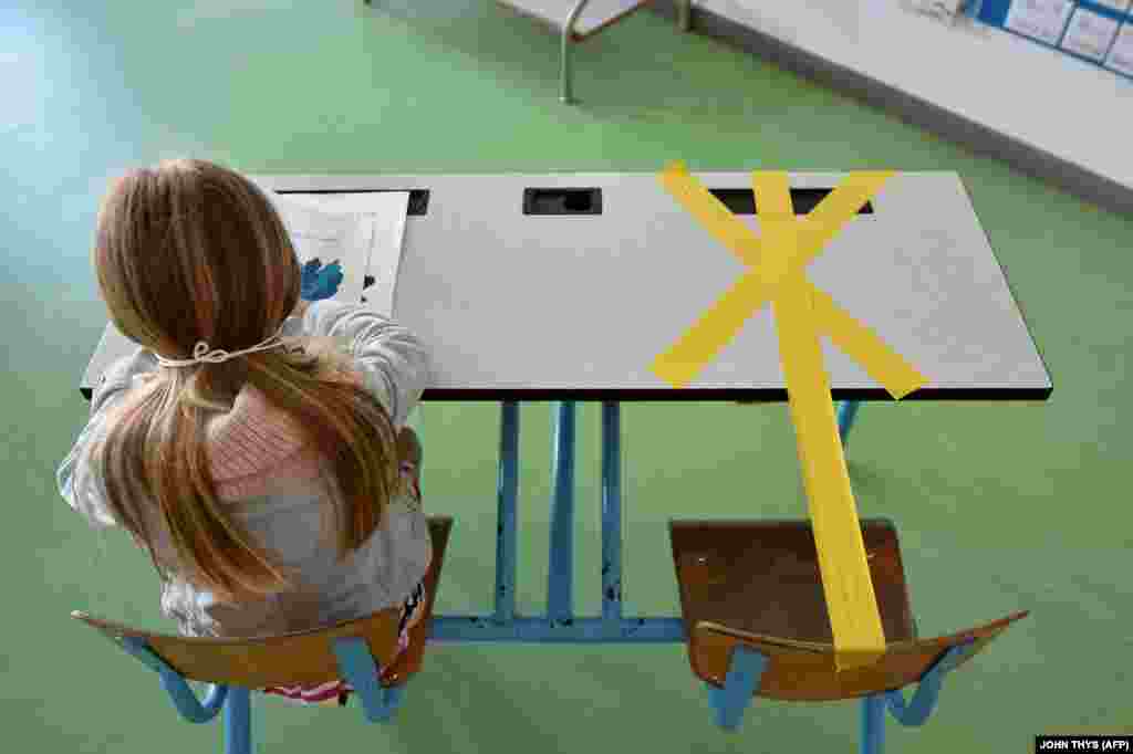 Учениця початкової школи Сент-Круа в місті Анню в Бельгії працює 15 травня 2020 року на своїй половині парти, а інша її половина заклеєна стрічкою, щоб забезпечити безпечну відстань для боротьби з розповсюдженням захворювання COVID-19, спричиненим новим коронавірусом