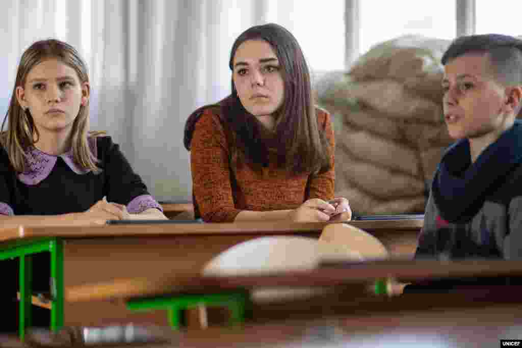 Зруйновані класи, вікна, закладені мішками з піском, щоб захищати дітей від випадкових куль – не найкраще місце для навчання. Проте більшість шкіл вздовж лінії розмежування на Донбасі мають такі інтер’єри. Марії (у центрі фото) 13 років, вона також навчається у Мар’їнській школі. Дівчина розповідає, що у 2014 році їй ледве вдалося врятуватися від обстрілу. Її матері наснився поганий сон, і вона вирішила, що в ту ніч потрібно заночувати в бабусі. «Того ж дня в наш будинок влучив снаряд. Ми там більше не живемо», – пригадує школярка.