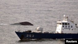 A maritime police ship patrols to rescue possible survivors of the sunken naval ship, seen in the background.