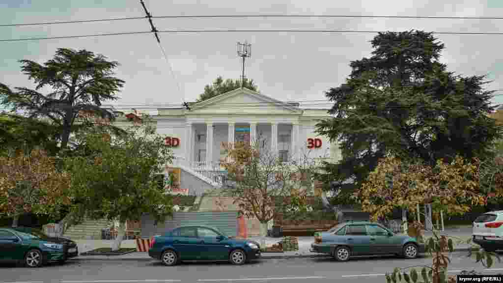 За многолетними деревьями расположен центральный кинотеатр Севастополя – «Победа»