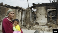 An ethnic Uzbek woman on June 16 carries her child past homes destroyed during the clashes in her village, Kyr-Aryk in the Osh region.