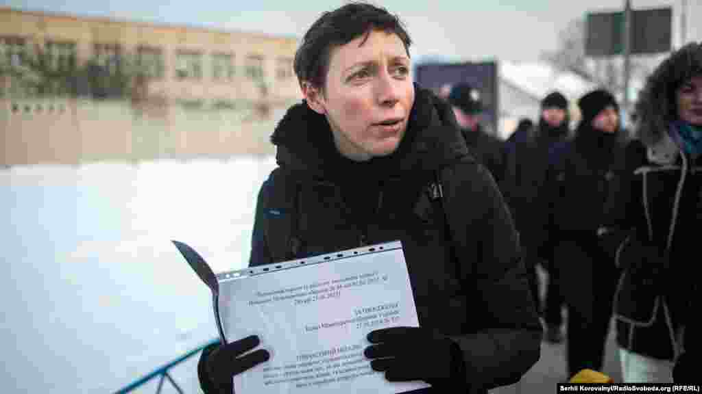 Учасниця ходи тримає в руках папери, що засвідчують на законодавчому рівні статеву дискримінацію жінок в армії. Зокрема, кількість посад, які може обіймати жінка в армії, лишається мізерно малою: снайперки та гранатометниці офіційно зараховані «кухарками» чи «начальницями лазні»