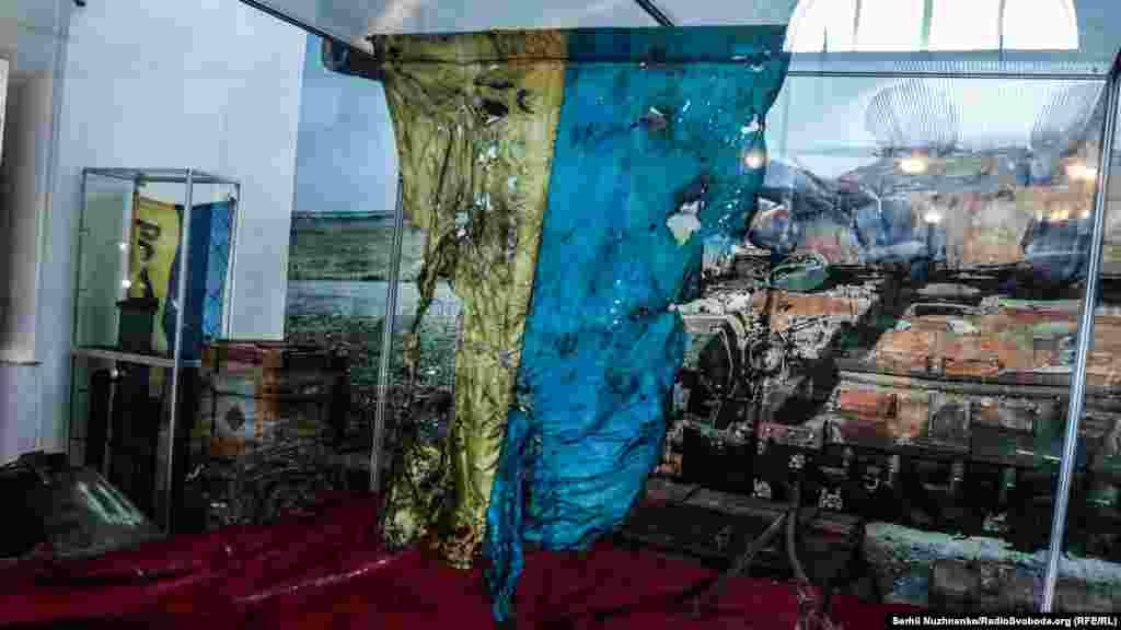 Государственный флаг Украины из «Иловайского котла». Флаг принадлежал бойцу 93-й отдельной механизированной бригады Александру Куренко. Флаг он получил в подарок от друга перед ротацией в зону АТО. Изуродованный флаг нашли в сгоревшей машине ЗИЛ во время поиска тел погибших